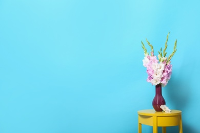 Photo of Vase with beautiful gladiolus flowers on wooden table against blue background. Space for text