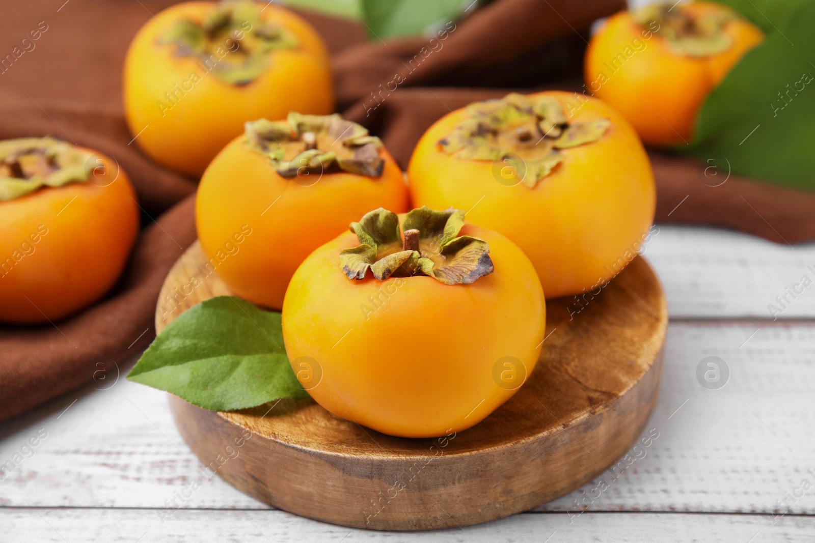 Photo of Delicious ripe juicy persimmons on white wooden table, closeup