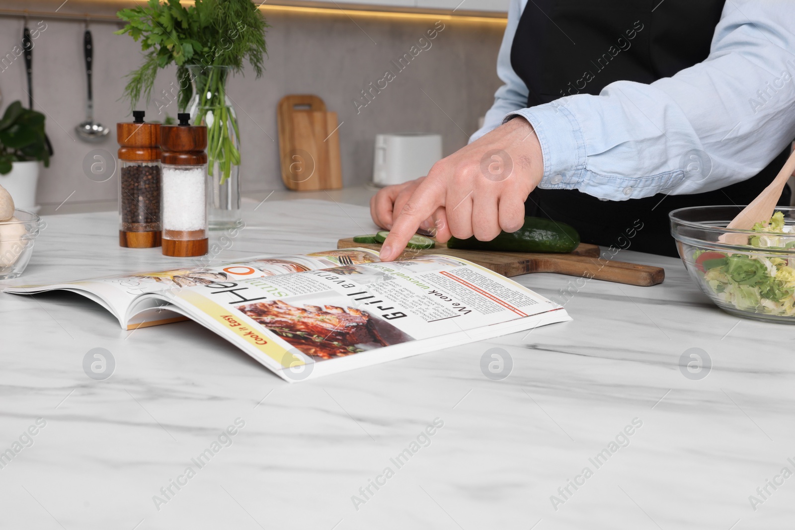 Photo of Man reading recipe in culinary magazine while cooking at home, closeup