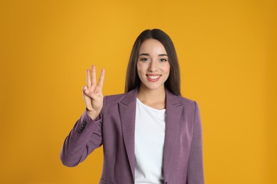 Photo of Woman in violet blazer showing number three with her hand on yellow background