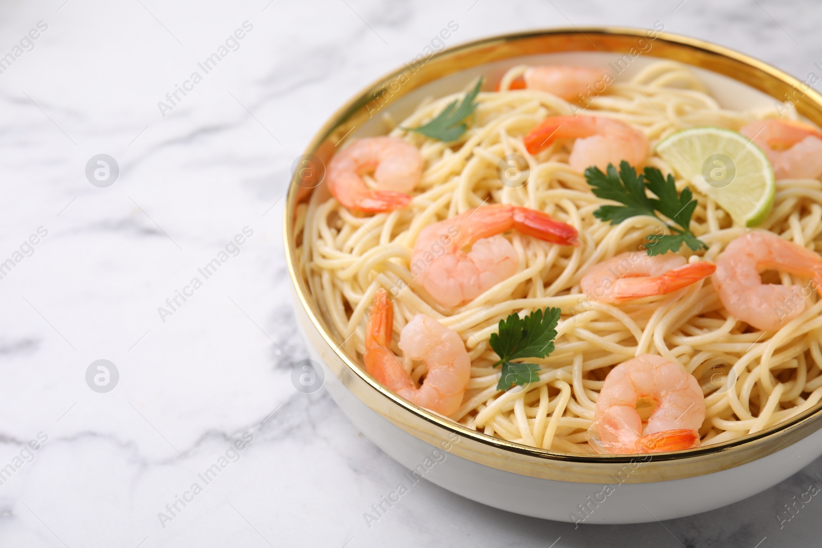 Photo of Tasty spaghetti with shrimps, lime and parsley in bowl on white marble table, closeup. Space for text