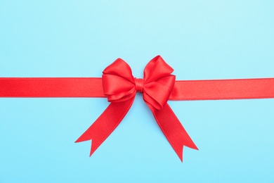 Photo of Red ribbon with bow on color background, top view