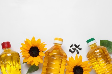Photo of Bottles of cooking oil, sunflowers and seeds on white table, flat lay. Space for text