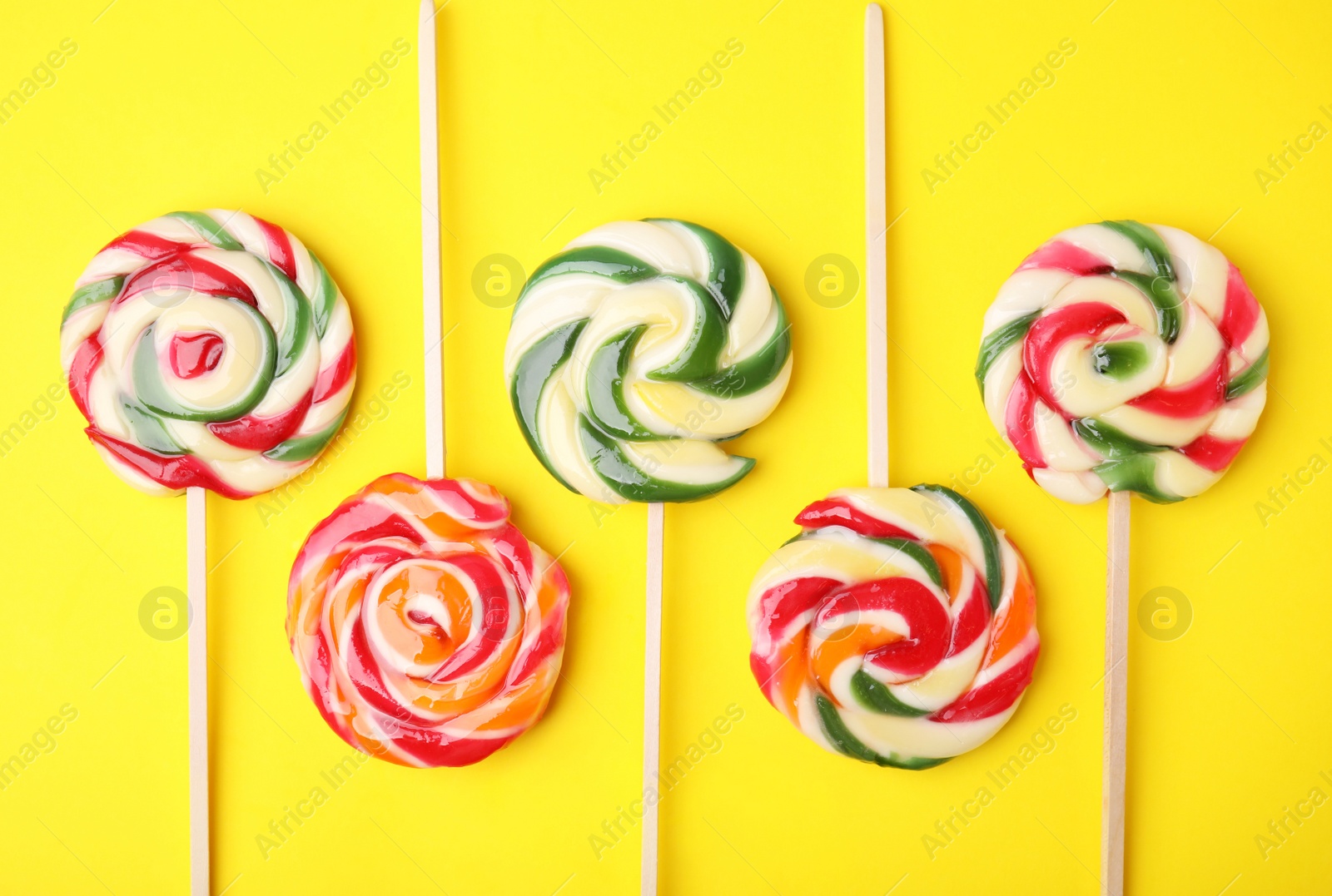 Photo of Many colorful lollipops on yellow background, flat lay