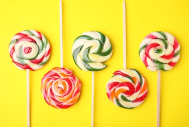 Many colorful lollipops on yellow background, flat lay