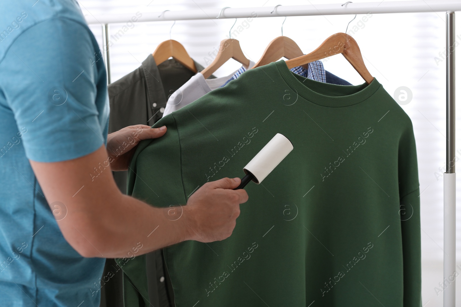 Photo of Man cleaning clothes with lint roller indoors, closeup