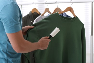 Photo of Man cleaning clothes with lint roller indoors, closeup