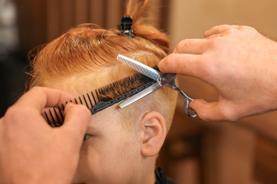 Professional hairdresser cutting boy's hair in beauty salon, closeup