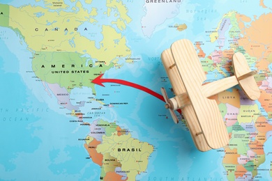 World map with wooden plane and red arrow pointing on USA, top view