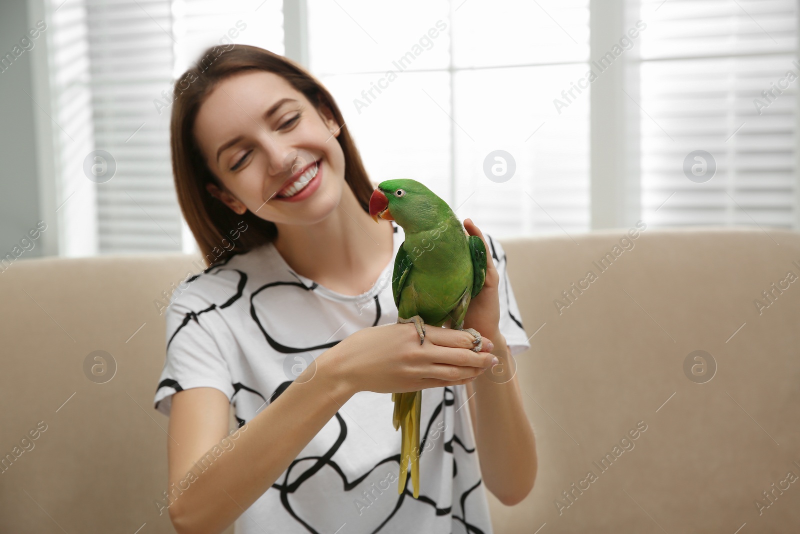 Photo of Young woman with cute Alexandrine parakeet indoors