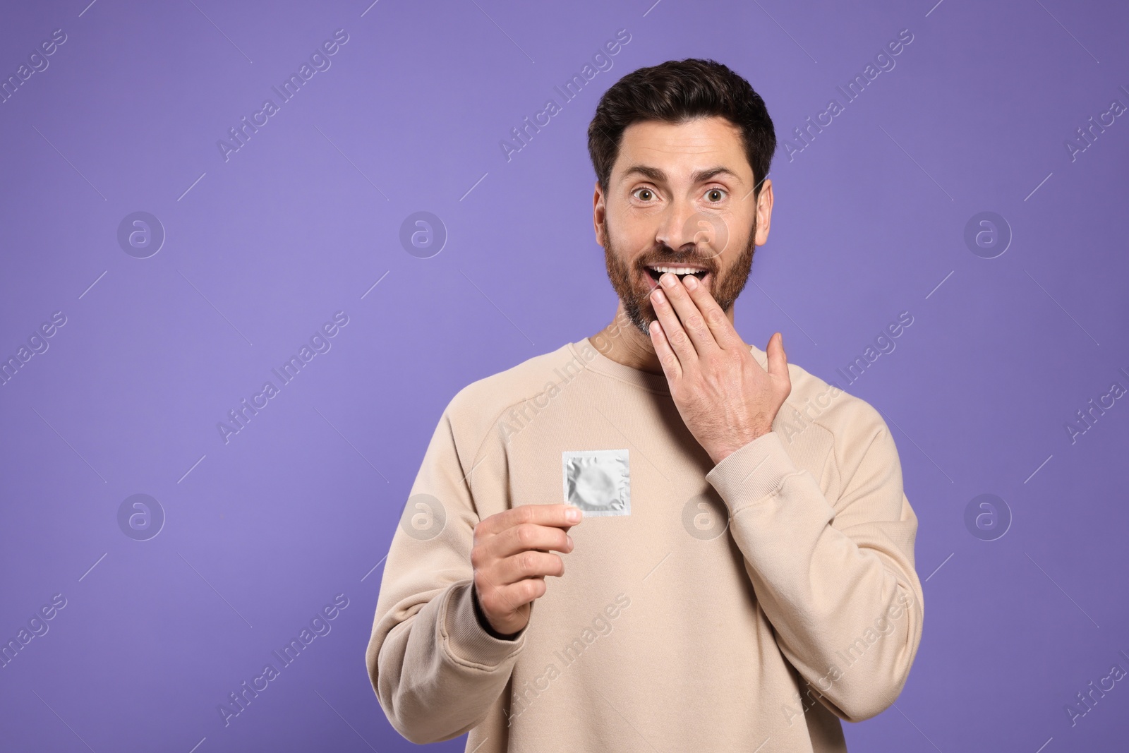 Photo of Emotional man holding condom on purple background, space for text. Safe sex