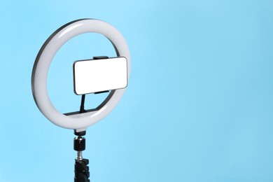 Modern tripod with ring light and smartphone on light blue background. Space for text