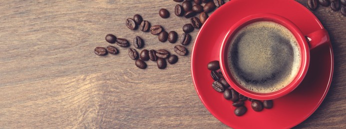 Cup of aromatic coffee and beans on wooden table, top view with space for text. Banner design