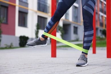 Woman doing exercise with fitness elastic band outdoors, closeup