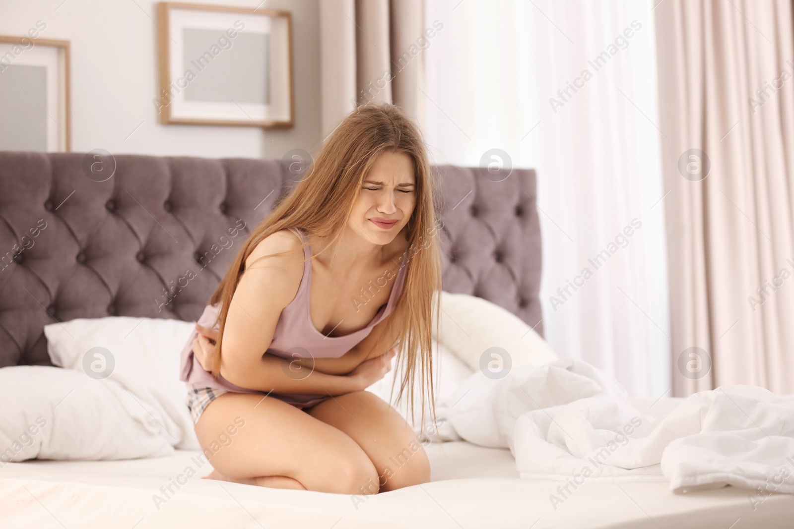 Photo of Young woman suffering from stomach ache in bedroom