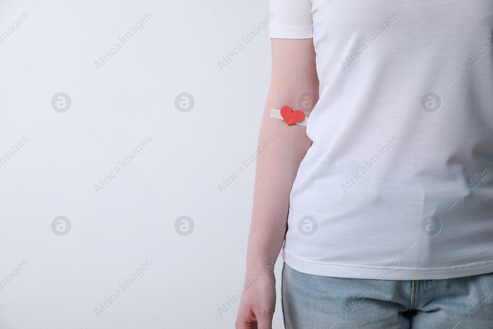 Photo of Blood donation concept. Woman with adhesive plaster on arm against white background, closeup. Space for text