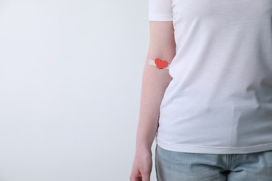 Blood donation concept. Woman with adhesive plaster on arm against white background, closeup. Space for text