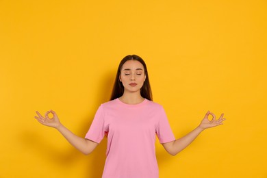Photo of Find zen. Beautiful young woman meditating on yellow background