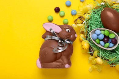 Flat lay composition with chocolate Easter bunny, eggs and candies on yellow background. Space for text