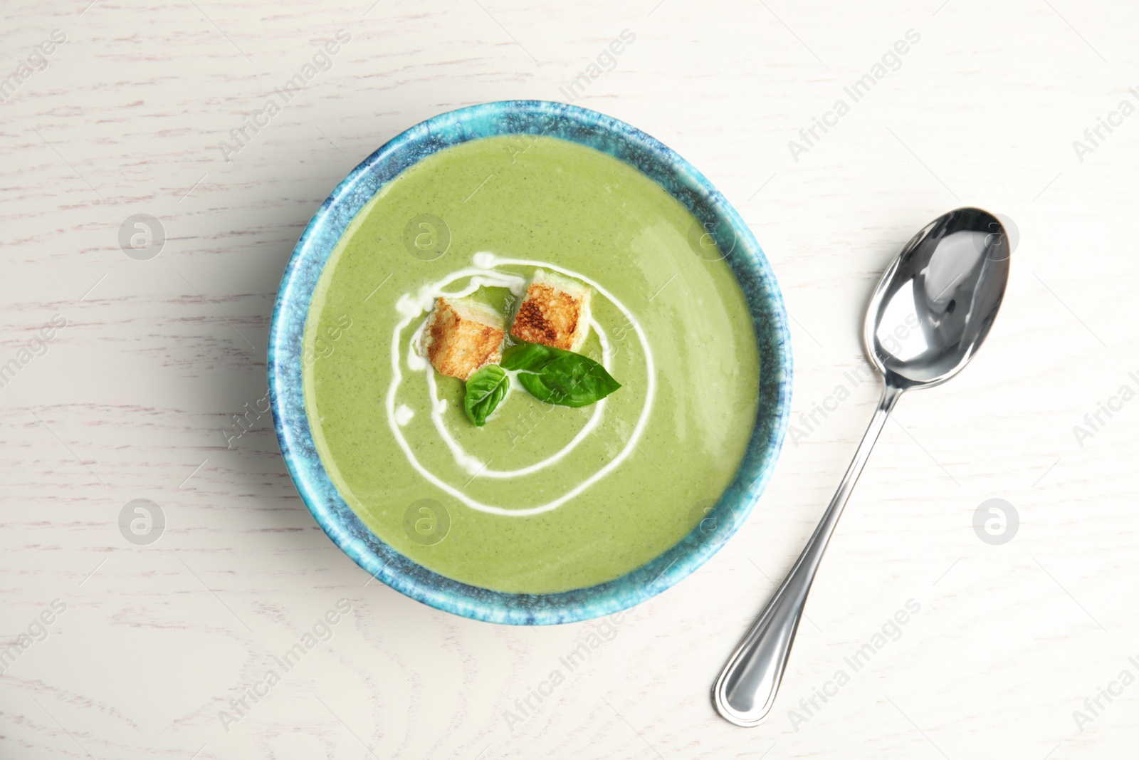 Photo of Delicious broccoli cream soup with croutons served on white wooden table, flat lay