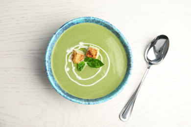 Photo of Delicious broccoli cream soup with croutons served on white wooden table, flat lay