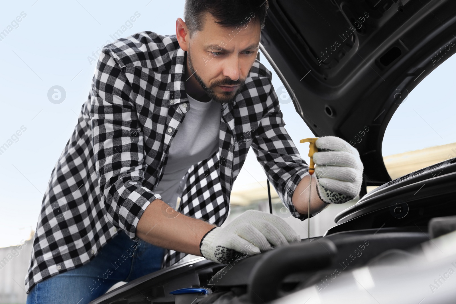 Photo of Man checking motor oil level with dipstick in car outdoors