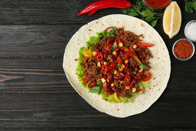 Photo of Delicious tortilla with meat on black wooden table, flat lay