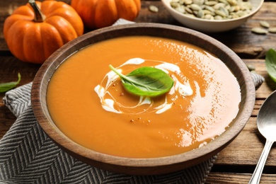 Photo of Tasty creamy pumpkin soup with basil in bowl on wooden table