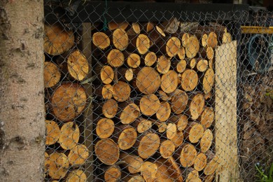 Photo of Stacked firewood behind wire mesh fence. Heating in winter