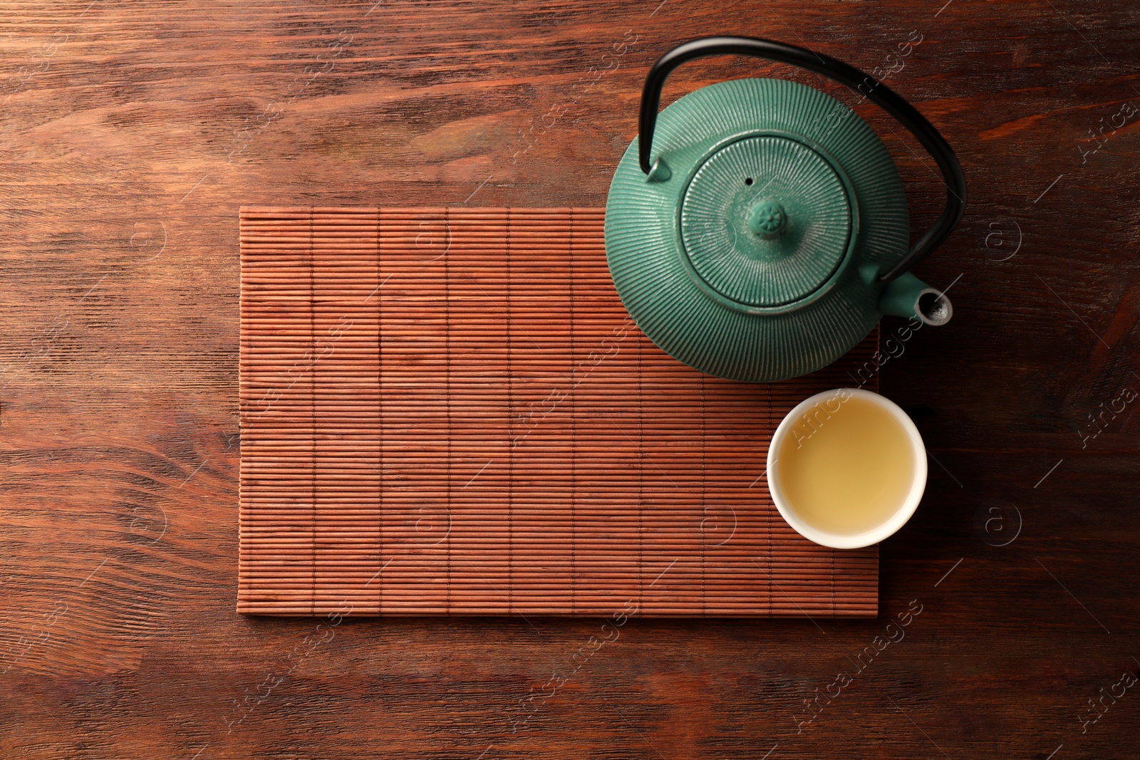 Photo of Bamboo mat, teapot and cup of tea on wooden table, top view. Space for text