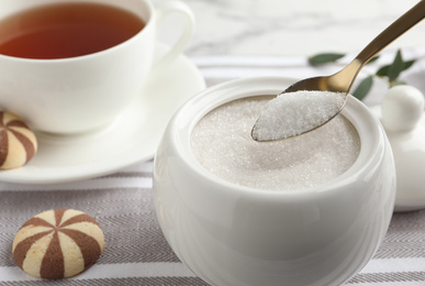 Photo of Spoon with granulated sugar over bowl on table