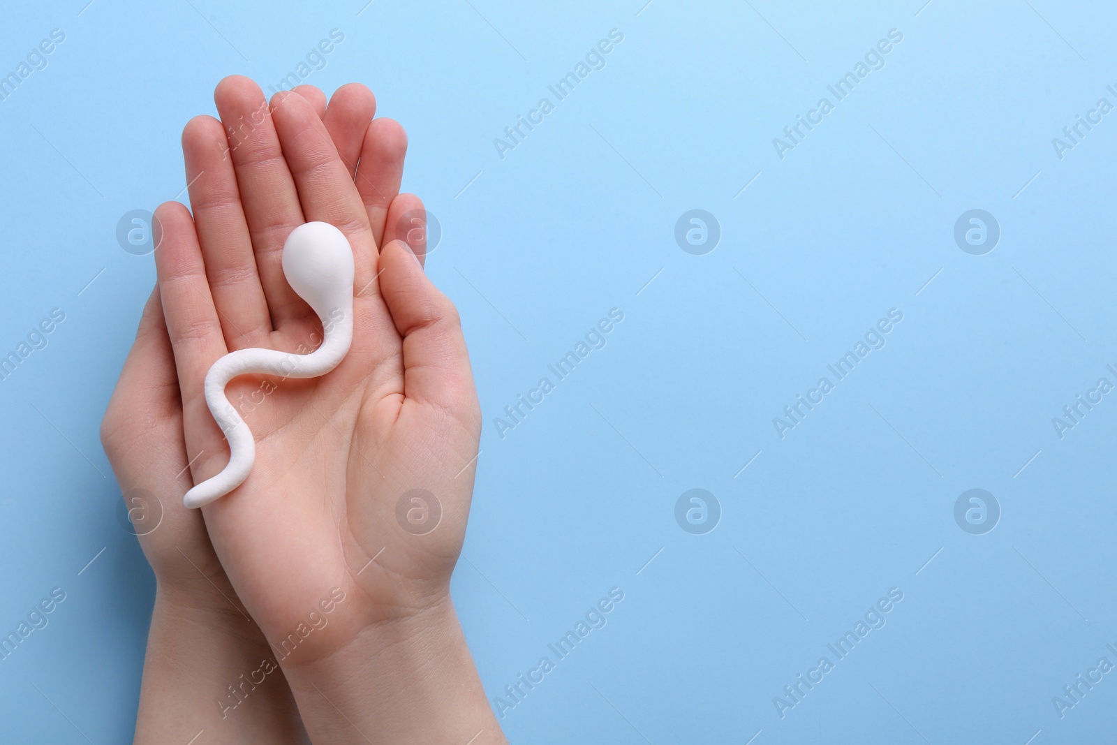 Photo of Reproductive medicine. Woman holding figure of sperm cell on light blue background, top view with space for text
