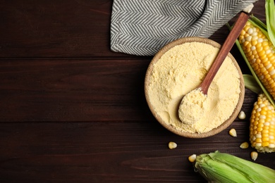 Corn flour in bowl and fresh cobs on wooden table, flat lay. Space for text