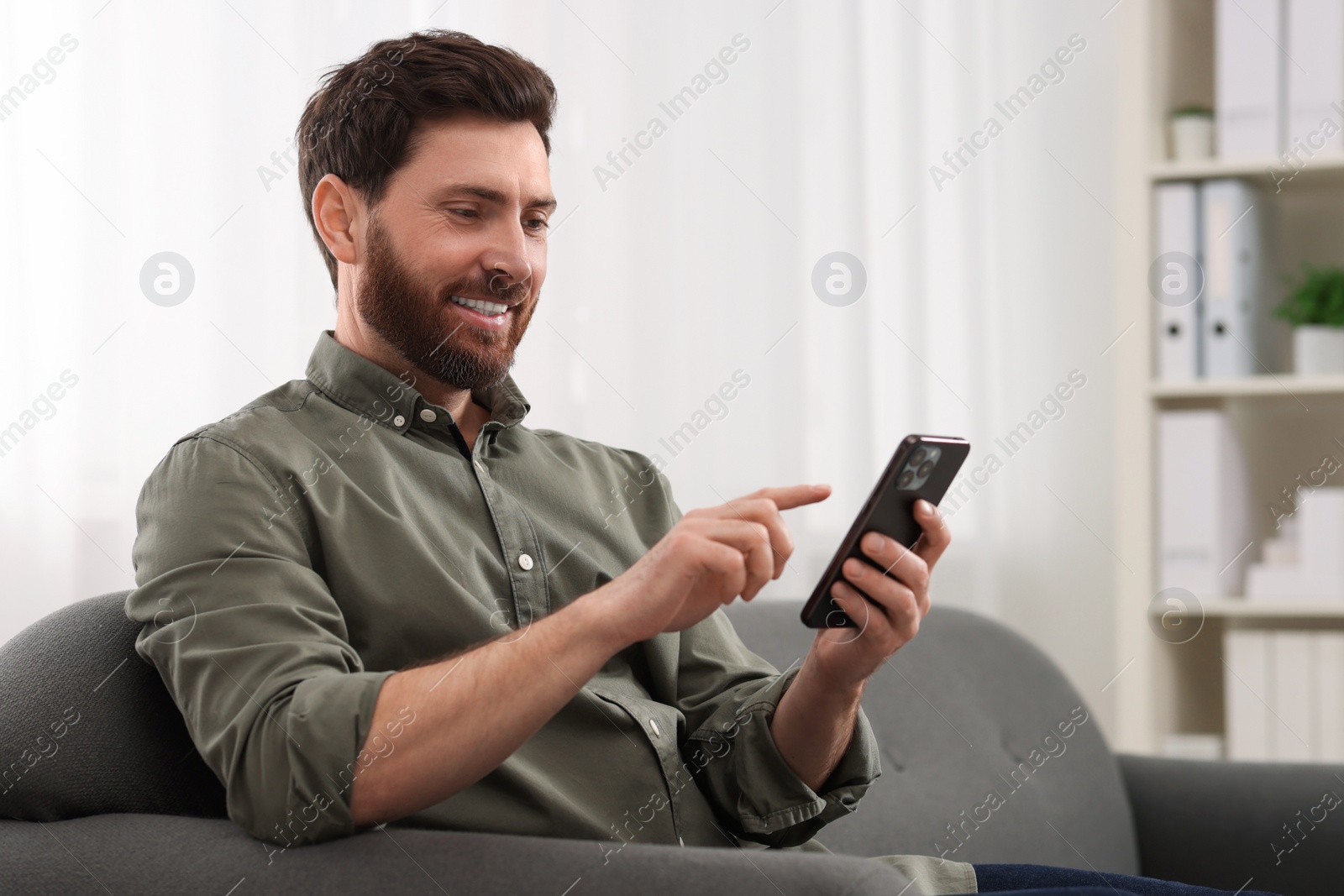 Photo of Smiling man using smartphone on sofa at home