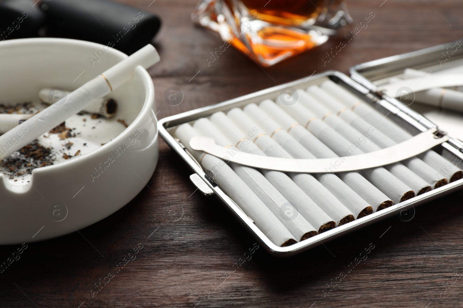 Photo of Open case with tobacco filter cigarettes and ashtray on wooden table, closeup