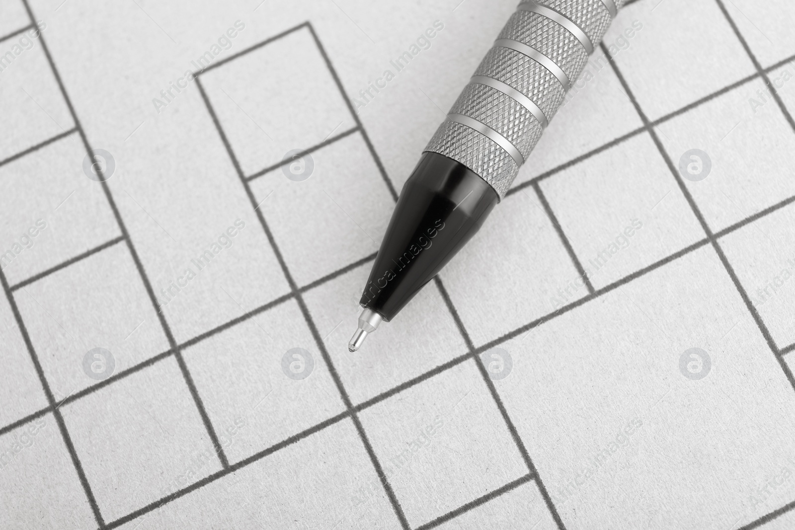 Photo of Pen on blank crossword, top view. Intellectual entertainment