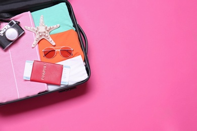 Photo of Open suitcase with beach objects on pink background, top view. Space for text