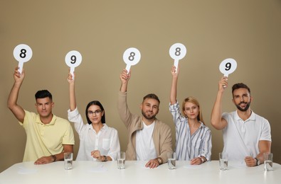 Panel of judges holding different score signs at table on beige background