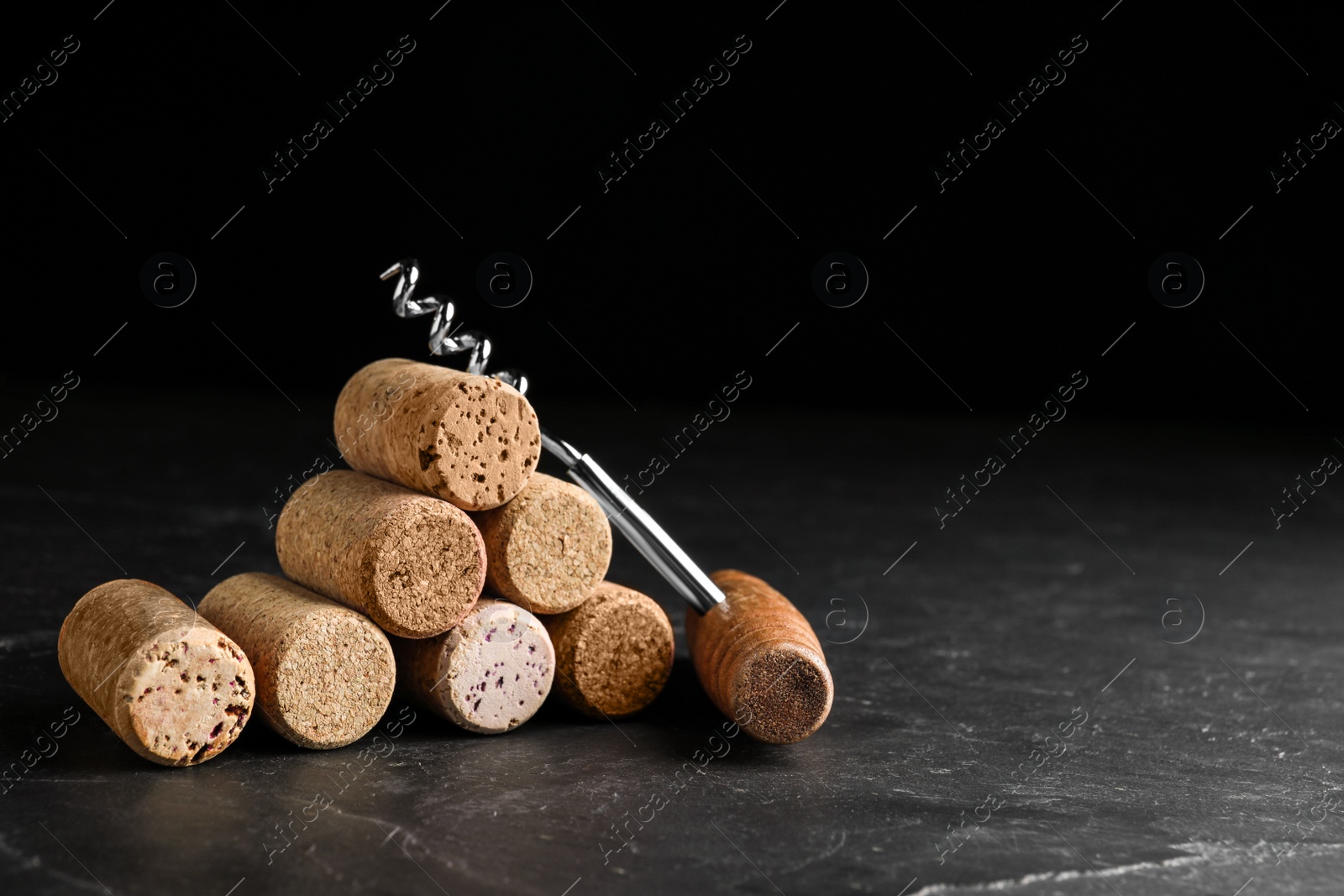 Photo of Corkscrew and stack of wine bottle stoppers on slate table. Space for text