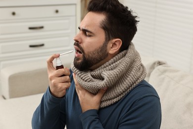 Young man with scarf using throat spray indoors