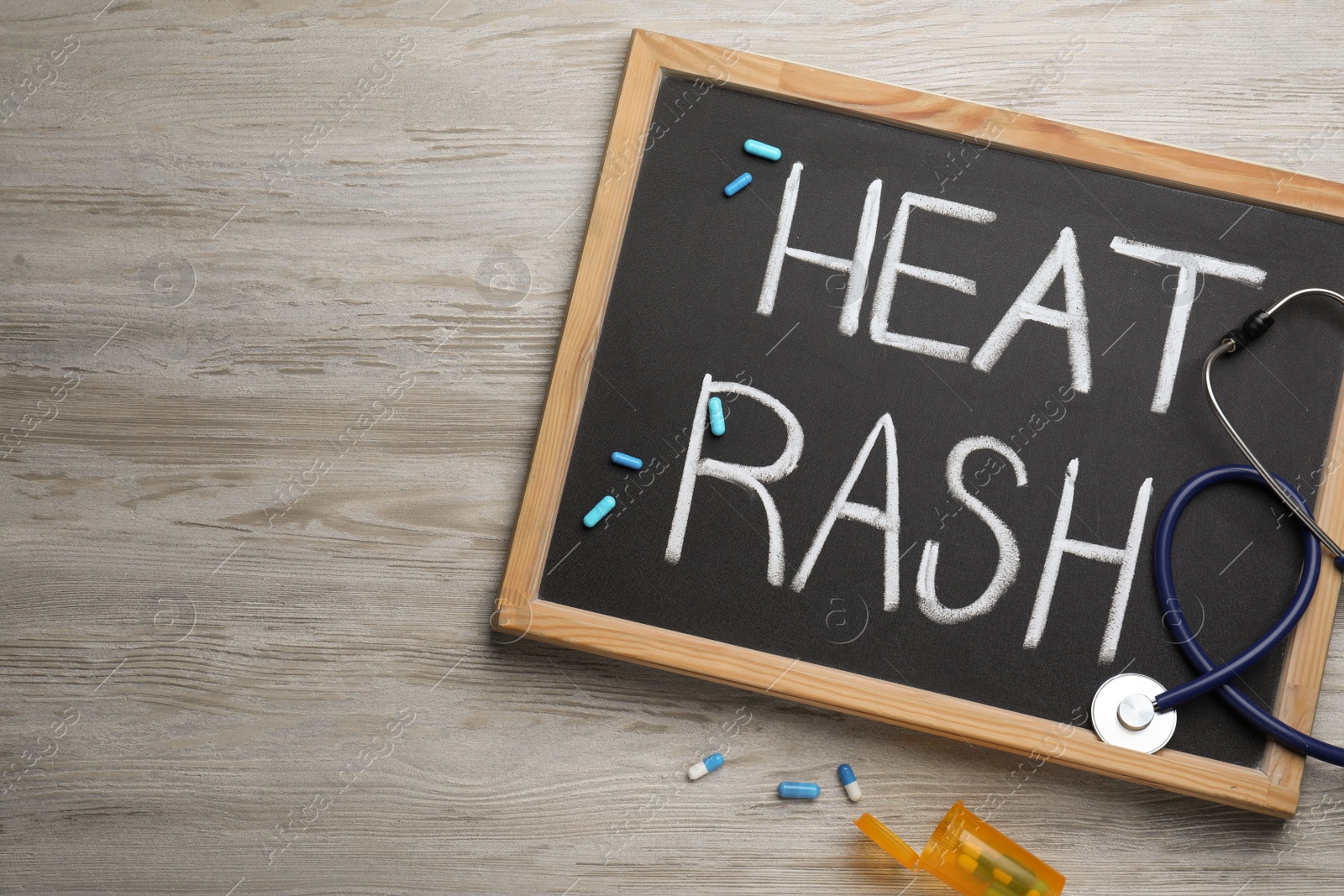 Photo of Blackboard with words Heat Rash, stethoscope and pills on wooden table, flat lay. Space for text