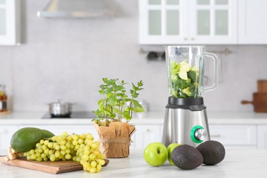 Photo of Blender with many ingredients for smoothie on white table in kitchen