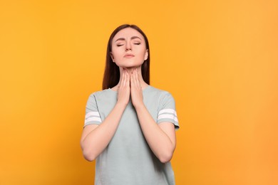 Photo of Young woman with sore throat on orange background