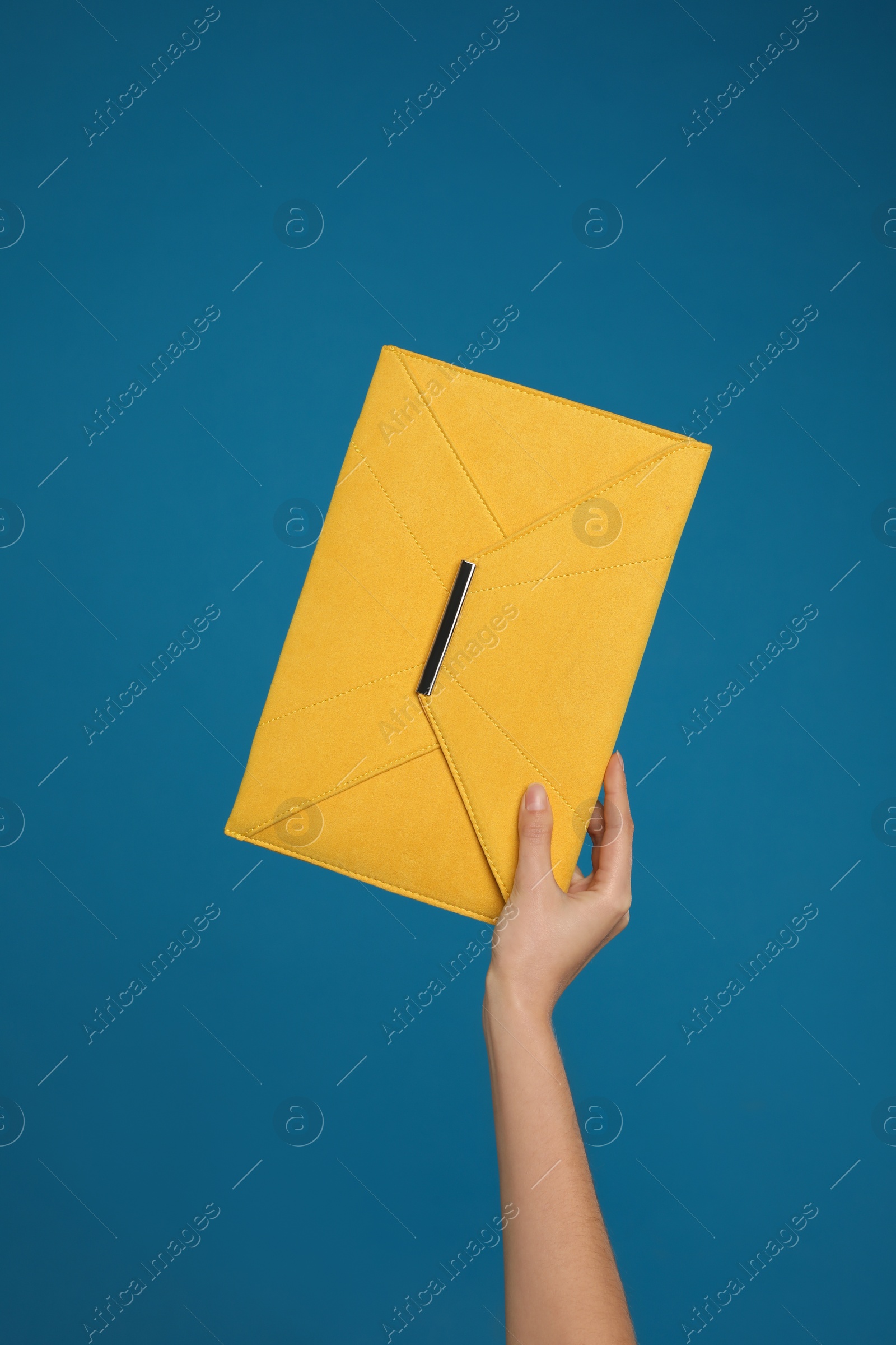 Photo of Woman holding stylish envelope bag on blue background, closeup