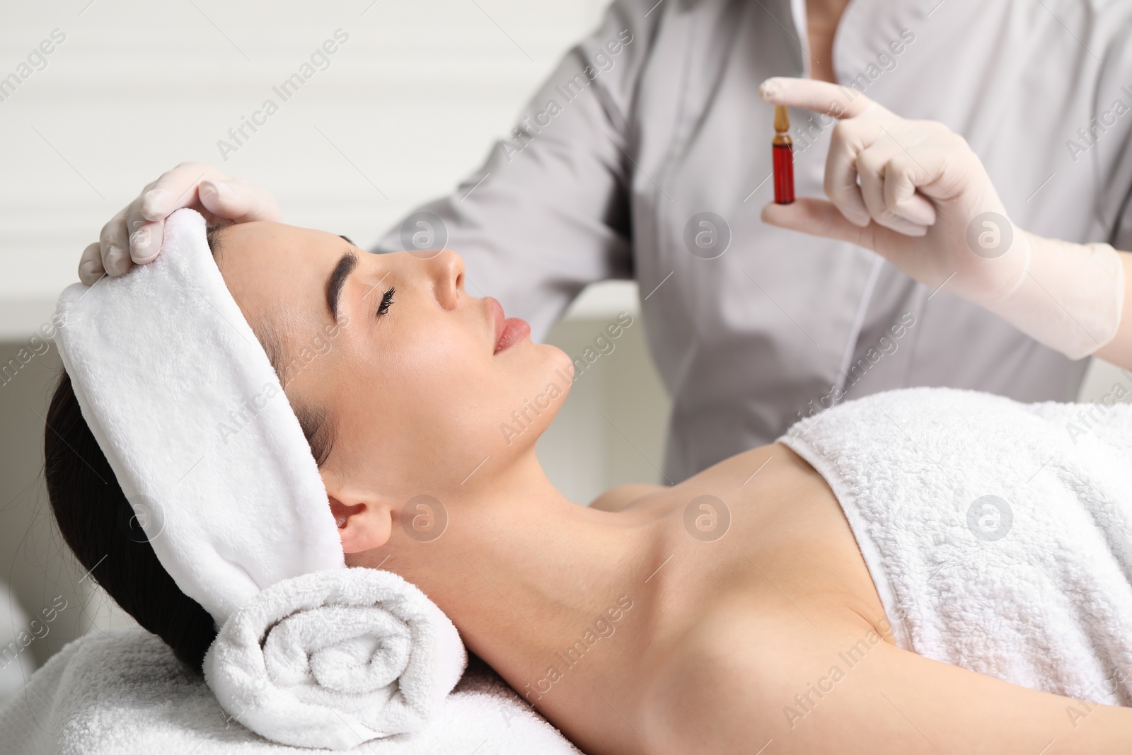 Photo of Professional cosmetologist holding skincare ampoule while working with client in clinic, closeup