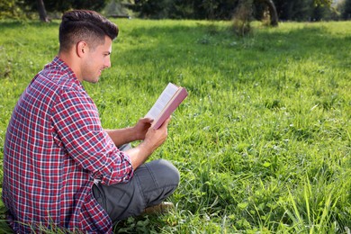 Man reading book on green grass outdoors