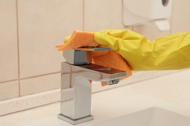 Photo of Person cleaning faucet with rag in bathroom, closeup