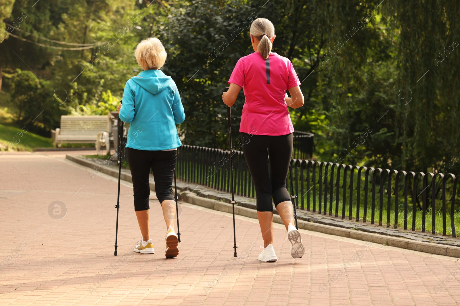 Photo of Two senior friends performing Nordic walking outdoors, back view