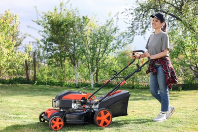 Smiling woman cutting green grass with lawn mower in garden