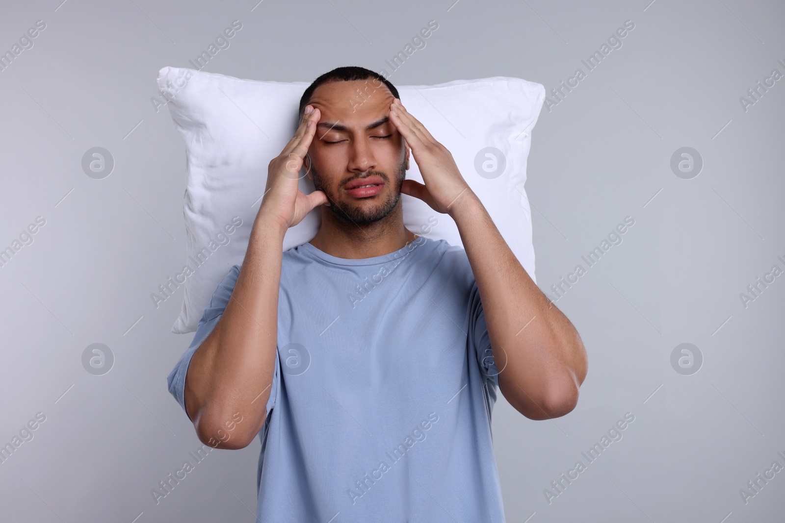 Photo of Tired man with pillow on light grey background. Insomnia problem